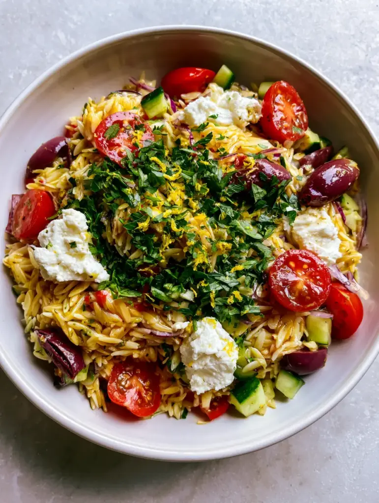 Close-up of rustic feta crumbles and cherry tomatoes in a Mediterranean orzo salad. (orzo salad)