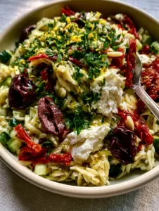Close up of al dente Orzo Pasta Salad showing a shimmering lemon-herb vinaigrette and julienned sun-dried tomatoes.