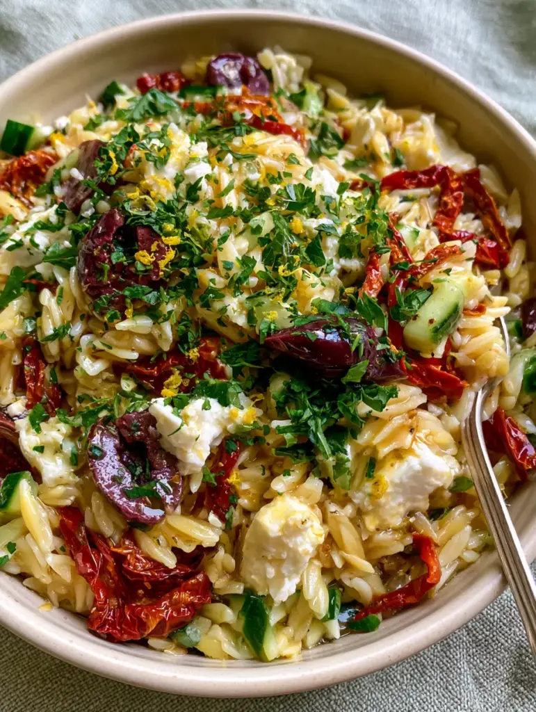 A silver spoon lifting a 'perfect bite' of Orzo Pasta Salad with feta, cucumber, and kalamata olives.