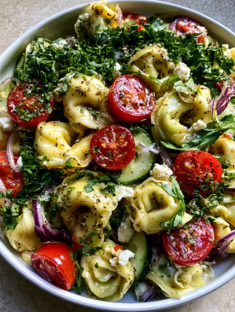 Extreme close-up of glossy cheese tortellini and bright red cherry tomatoes in a cold tortellini pasta salad.
