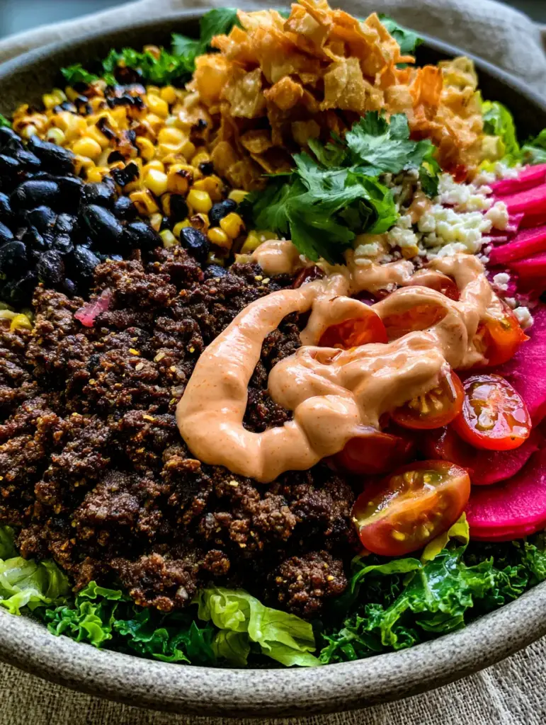 Extreme close-up of a thick ribbon of pale-orange chipotle dressing over charred corn and heirloom tomatoes. (taco salad)