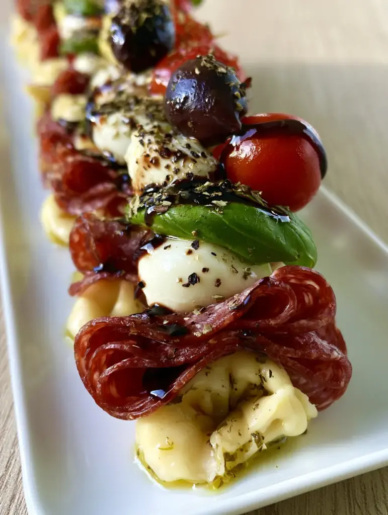 Vertical shot of several rows of gourmet antipasto skewers on a white ceramic platter against a light wood background.