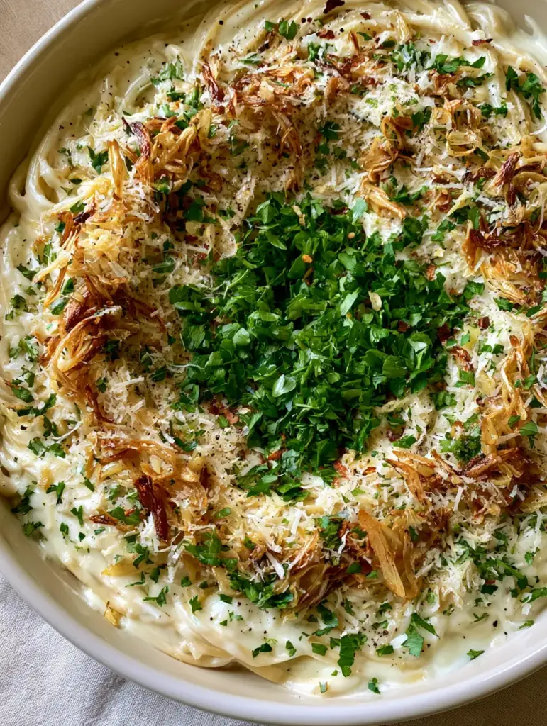 A shallow white ceramic skillet filled with garlic linguine topped with parsley and red pepper flakes.